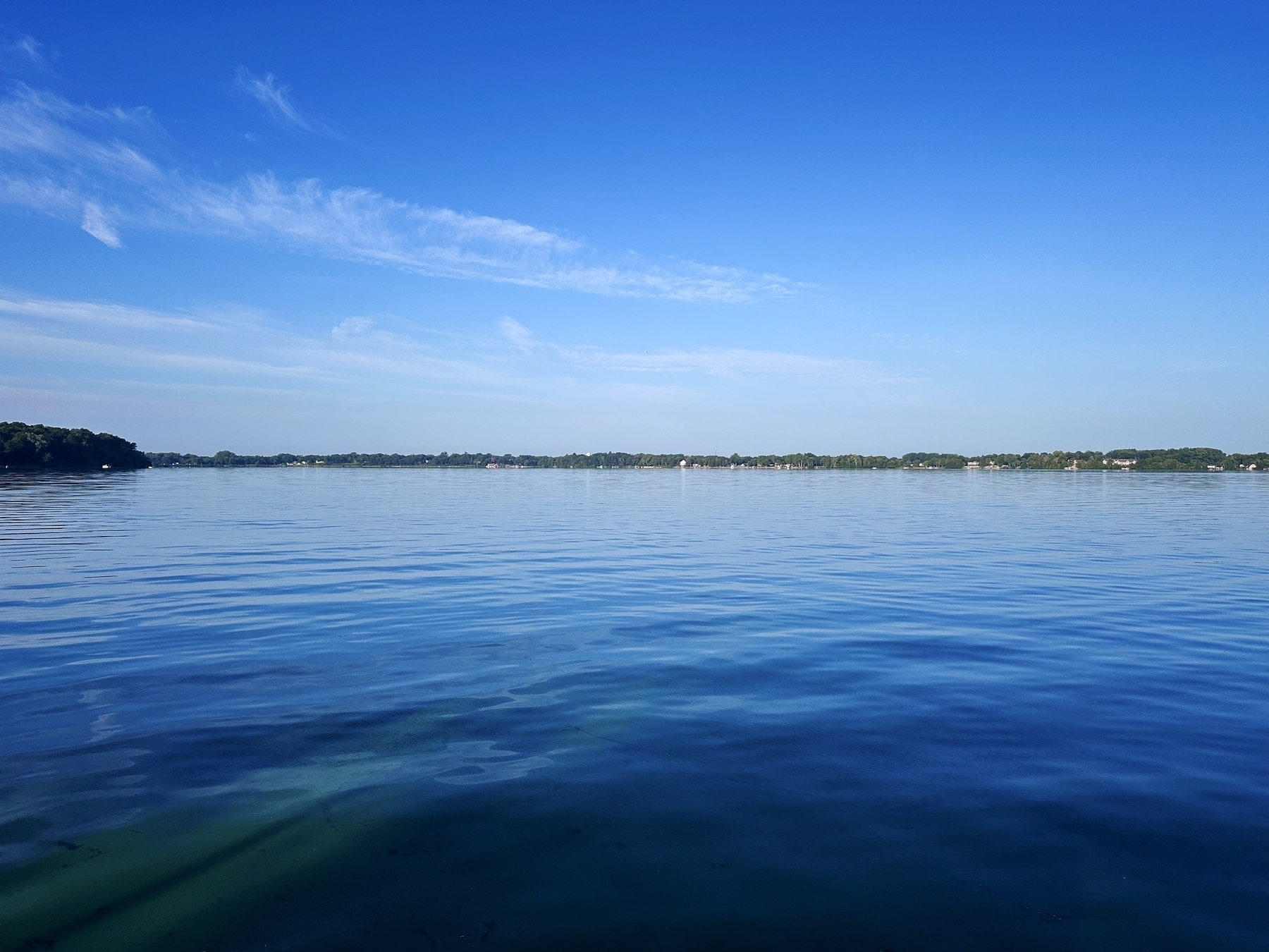 Still water reflects the clear blue sky with some wispy clouds, surrounded by distant greenery along the horizon.