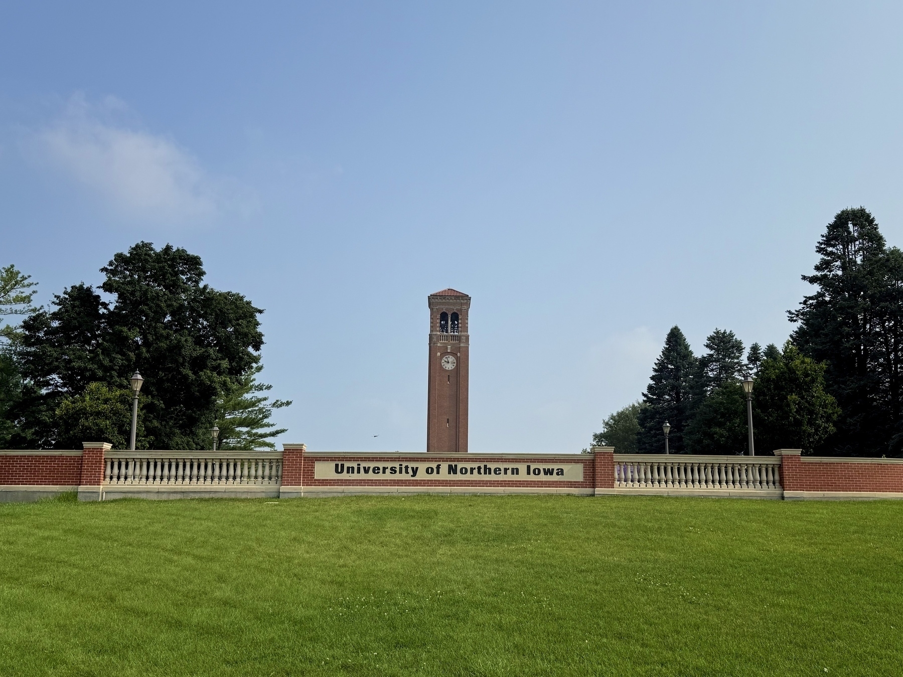 Clock tower at the University of Northern Iowa, surrounded by green grass and trees under a clear blue sky.